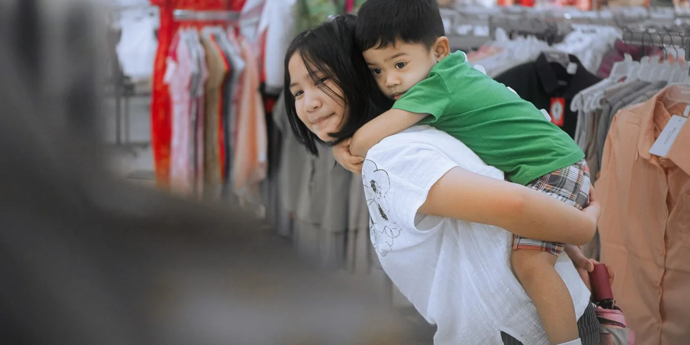 Parent browsing baby and kids clothing racks in retail store, selecting garments